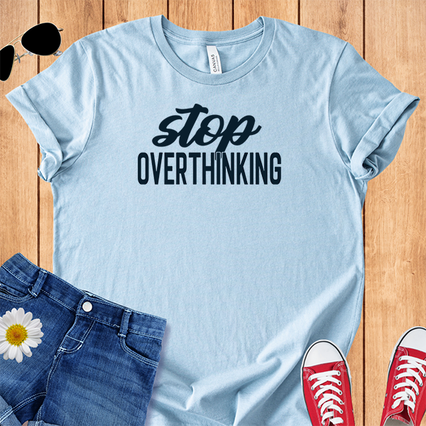 Light blue t-shirt with 'stop overthinking' text on a wooden surface with jeans, sneakers, and sunglasses.